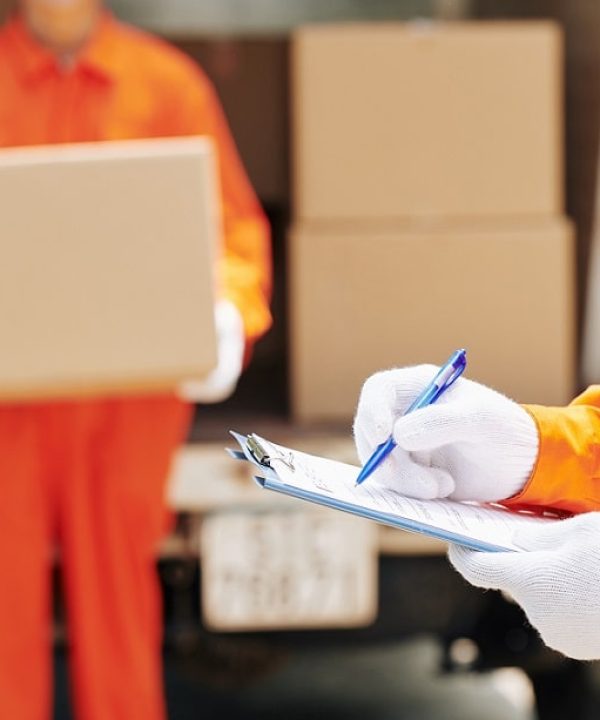 Unrecognizable moving man wearing orange uniform and white gloves holding clipboard with checklist paper making notes